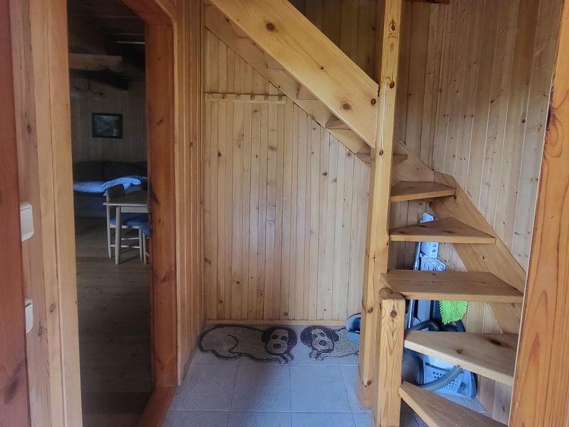 Drewniany przedpokój z drewnianymi schodami na piętro, obok otwarte drzwi do salonu