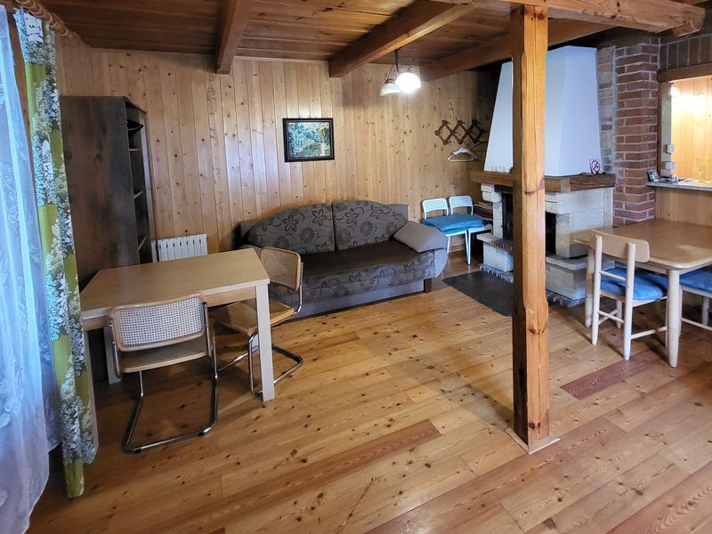 Drewniany salon z kanapą, stołami z krzesłami i białym kominkiem przy ceglanej ścianie