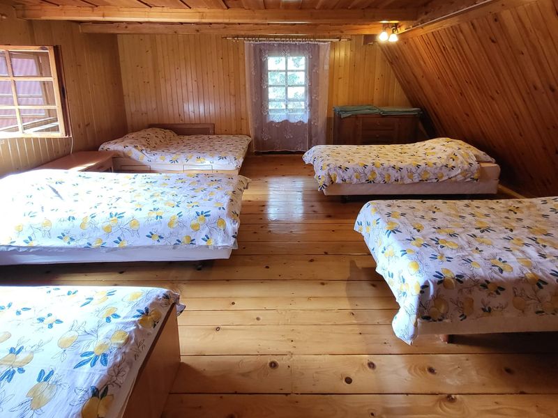Duża sypialnia na piętrze pod drewnianym skosem: pięć łóżek z pościelą w cytrynowy wzór